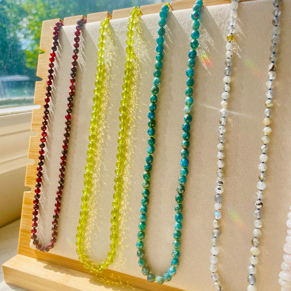 Set of beaded necklaces on a wooden stand with a blurred outdoor background