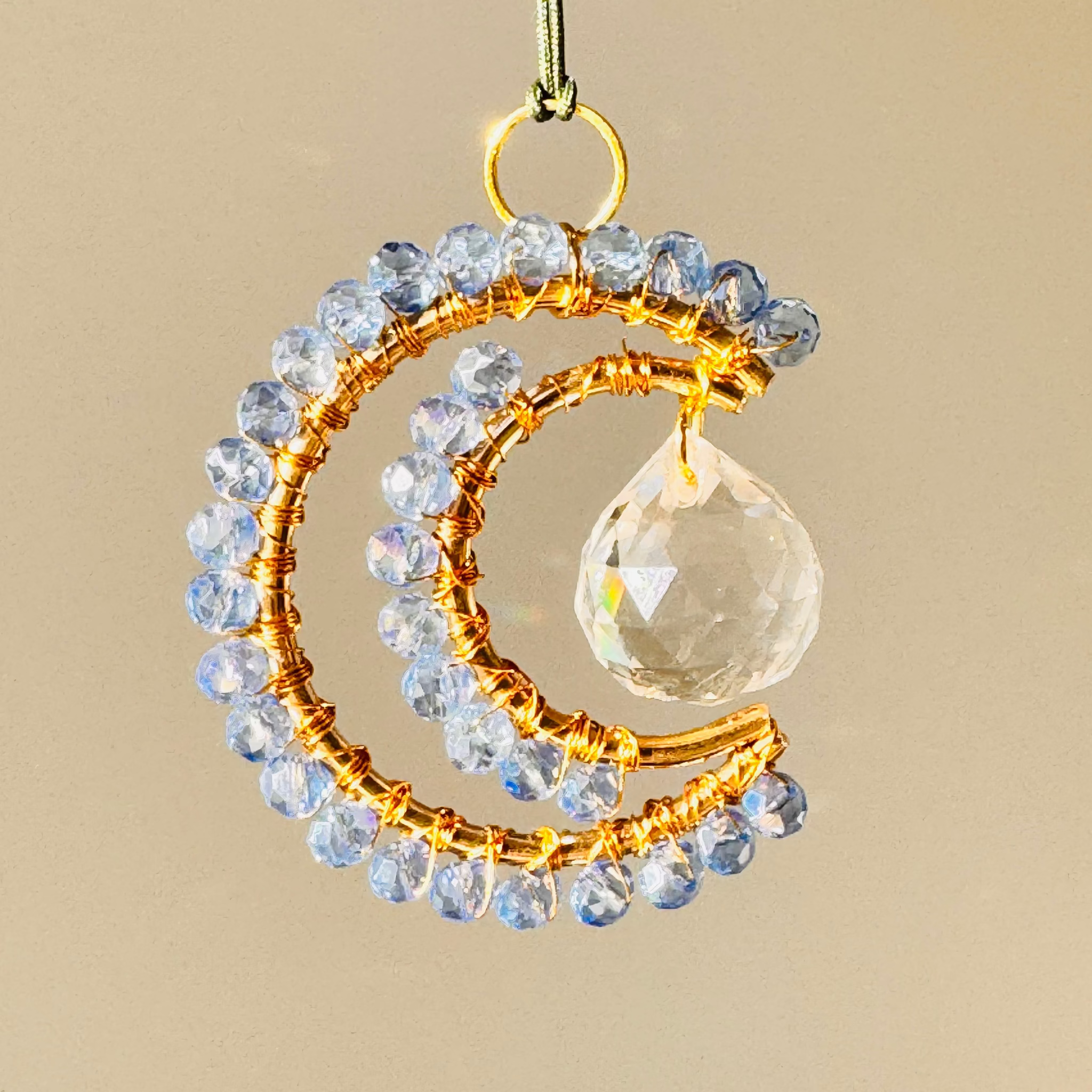 Decorative hanging ornament with crystal beads and a clear droplet on a beige background