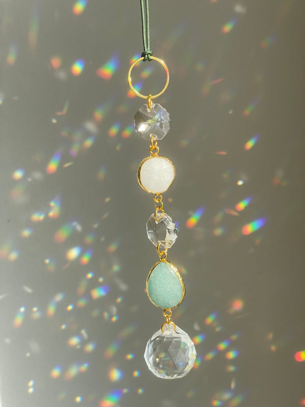 A string suncatcher with gold-colored frame and multiple clear and colored crystals, with a green loop for hanging.