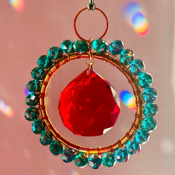 Decorative hanging ornament with red teardrop and green beads on a pink background