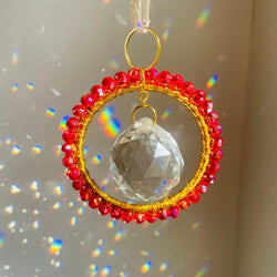 Decorative hanging ornament with red beads and a clear crystal ball on a neutral background