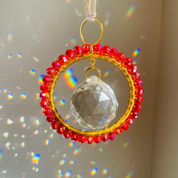 Decorative hanging ornament with red beads and a clear crystal ball on a neutral background