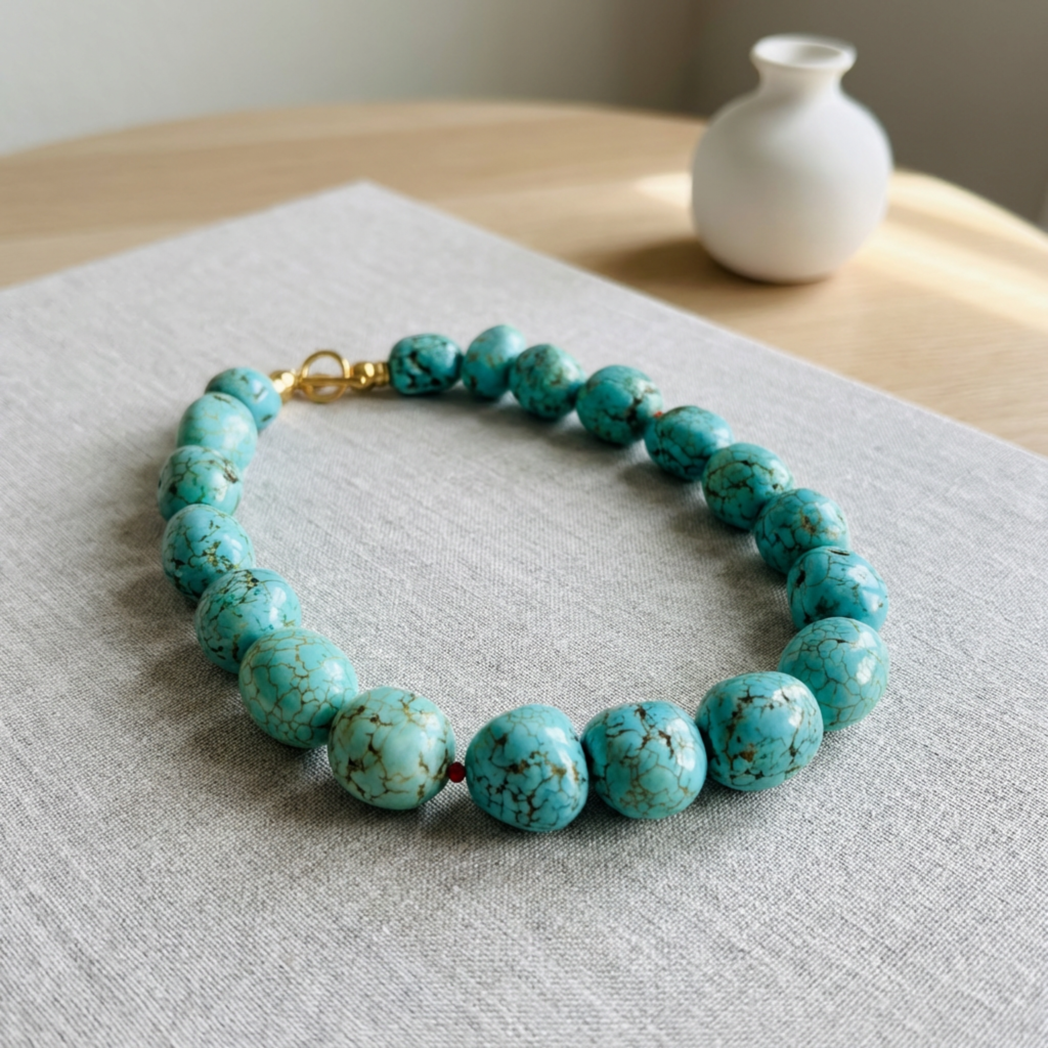 Turquoise beaded necklace on a light gray surface with a white vase in the background.