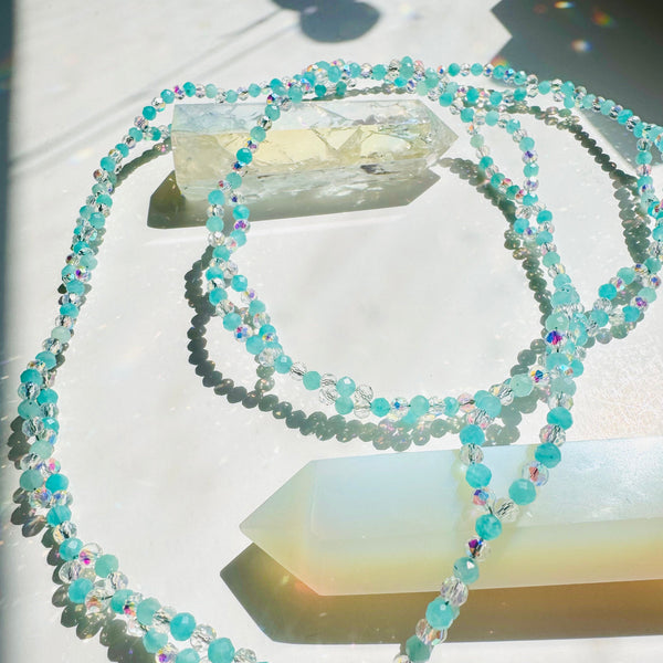 A tantric necklace featuring a series of round amazonite gemstones strung on a thread, with a larger gemstone at the center and smaller ones towards the ends.