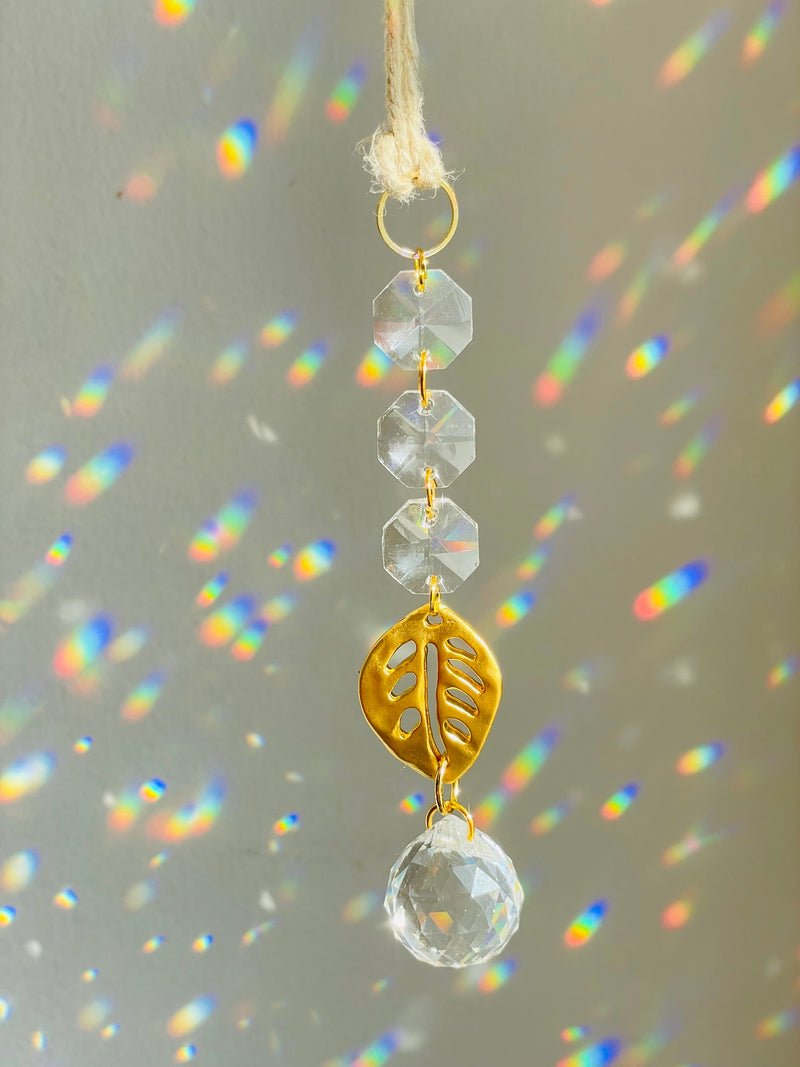 Decorative hanging ornament with crystals and gold leaf charm on a gray background