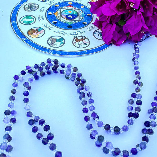 purple and clear gemstone beaded necklace on white surface decorated with pink flower
