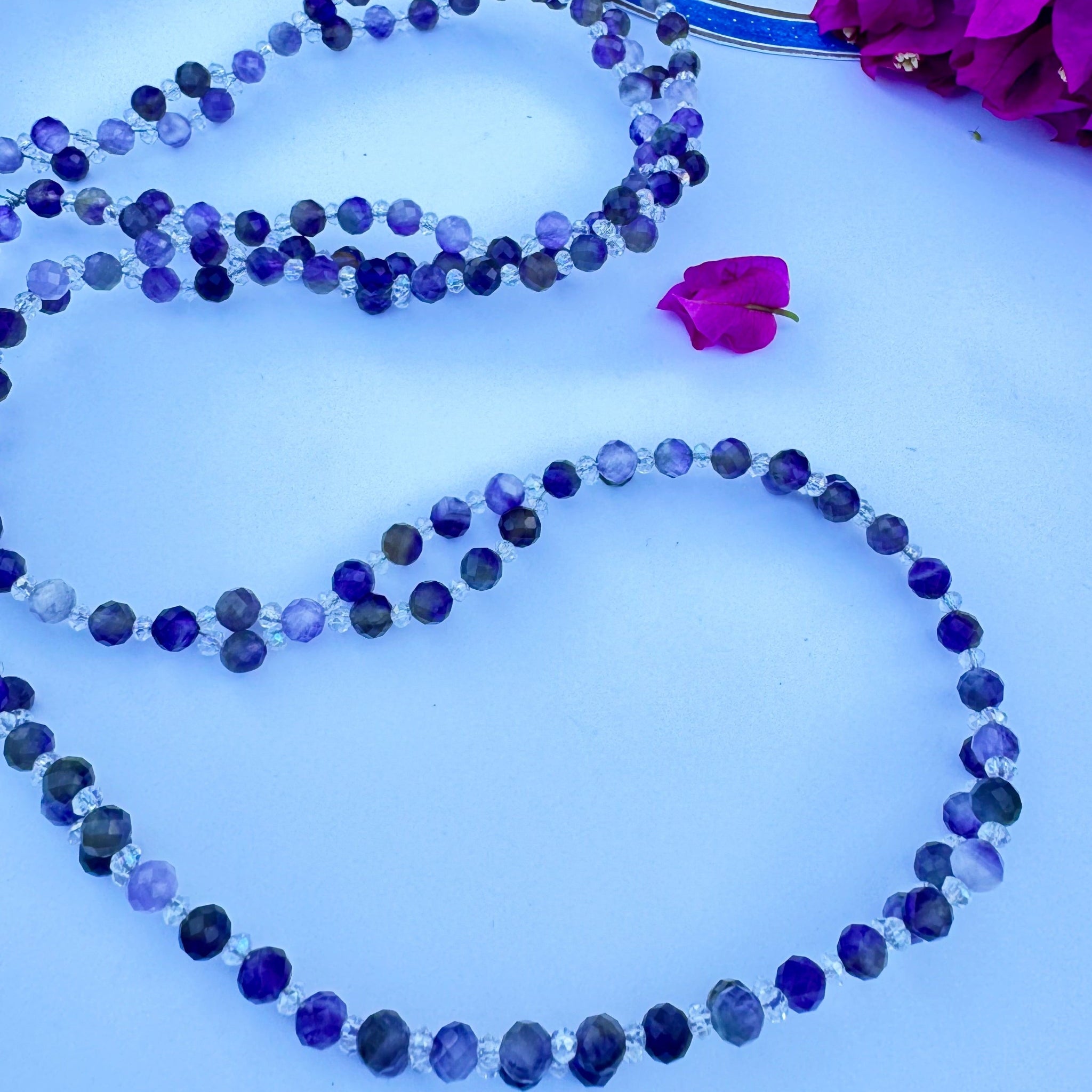 Purple beaded tantric necklace with pink flower decoration on white surface