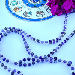 A tantric necklace with amethyst beads and a circular pendant featuring a sacred geometric pattern and a purple flower design.