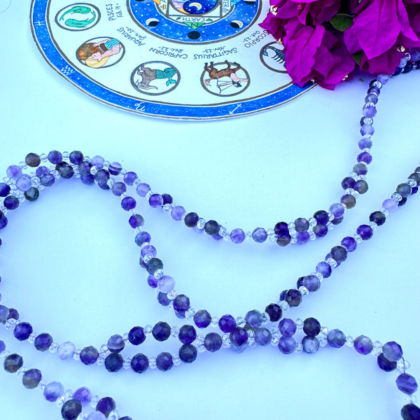 A tantric necklace with amethyst beads and a circular pendant featuring a sacred geometric pattern and a purple flower design.