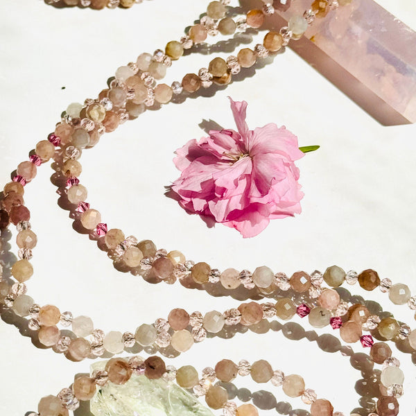 A close-up image of a Divine Love Morganite Tantric Necklace with intricate gemstone designs and a floral accent.