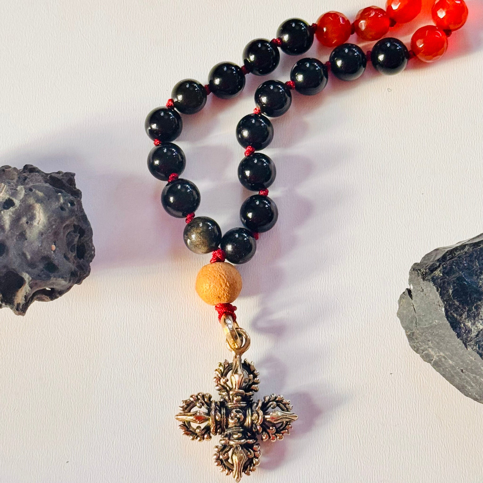 Beaded necklace with black, red, and gold beads and a cross pendant on a white background.