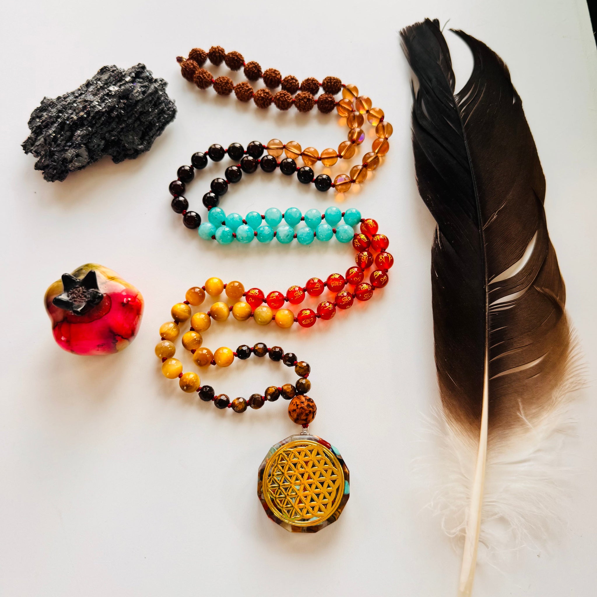 Collection of beaded necklaces, a feather, and a crystal on a white surface
