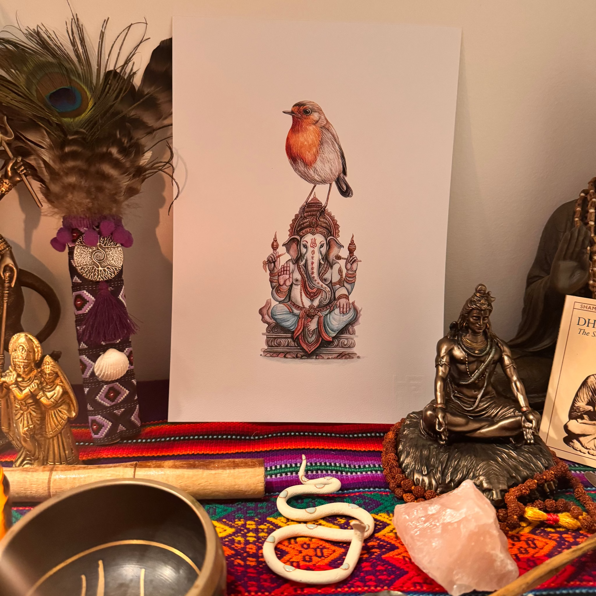 Decorative setup with statues, a painting of a bird on a deity, and a colorful rug.