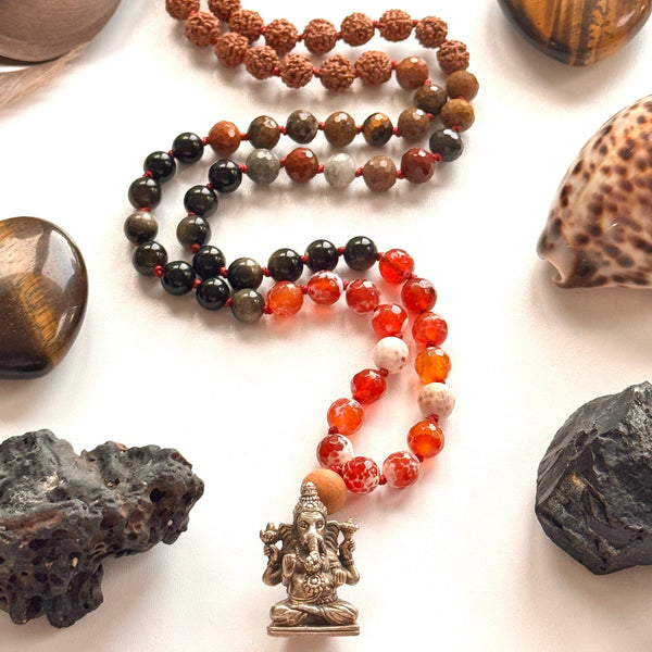 Necklace with various beads and a statue, surrounded by stones and shells on a white background