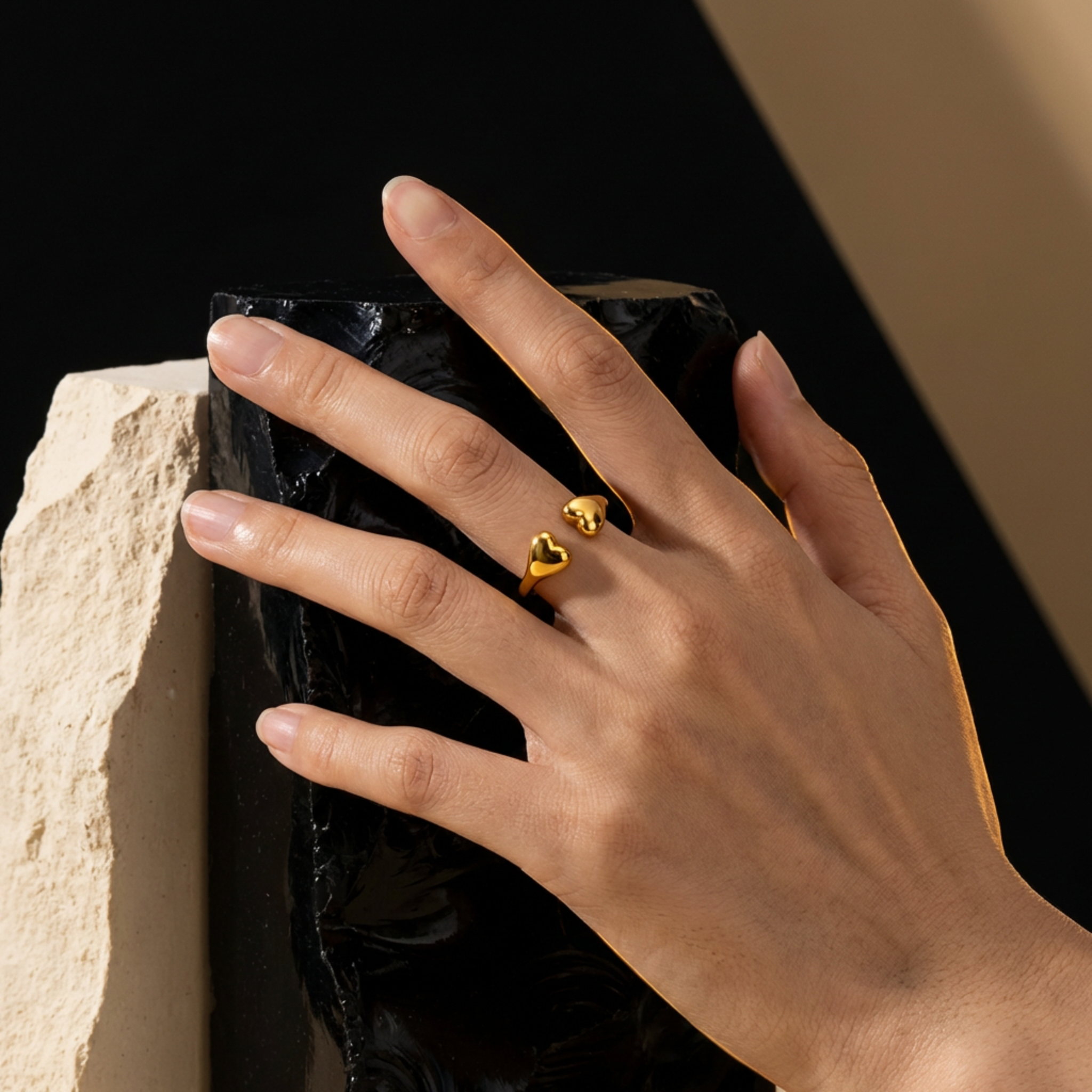 model wearing a gold dainty heart shaped ring on a black surface