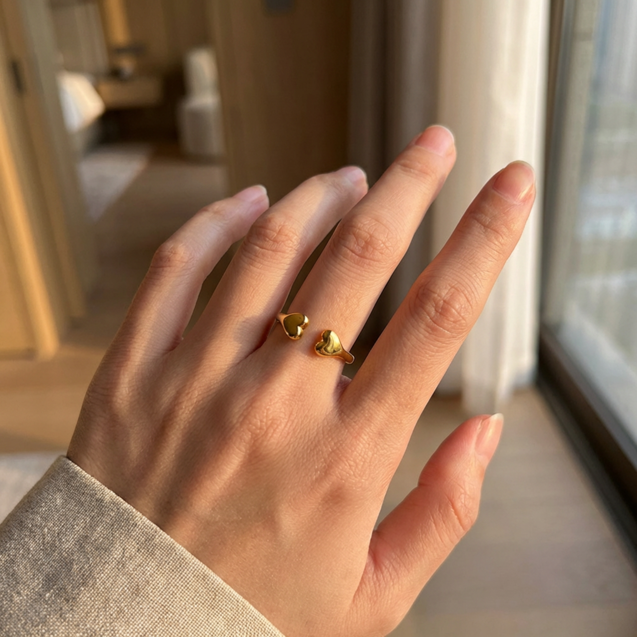 Hand wearing a gold heart-shaped ring in a softly lit room.