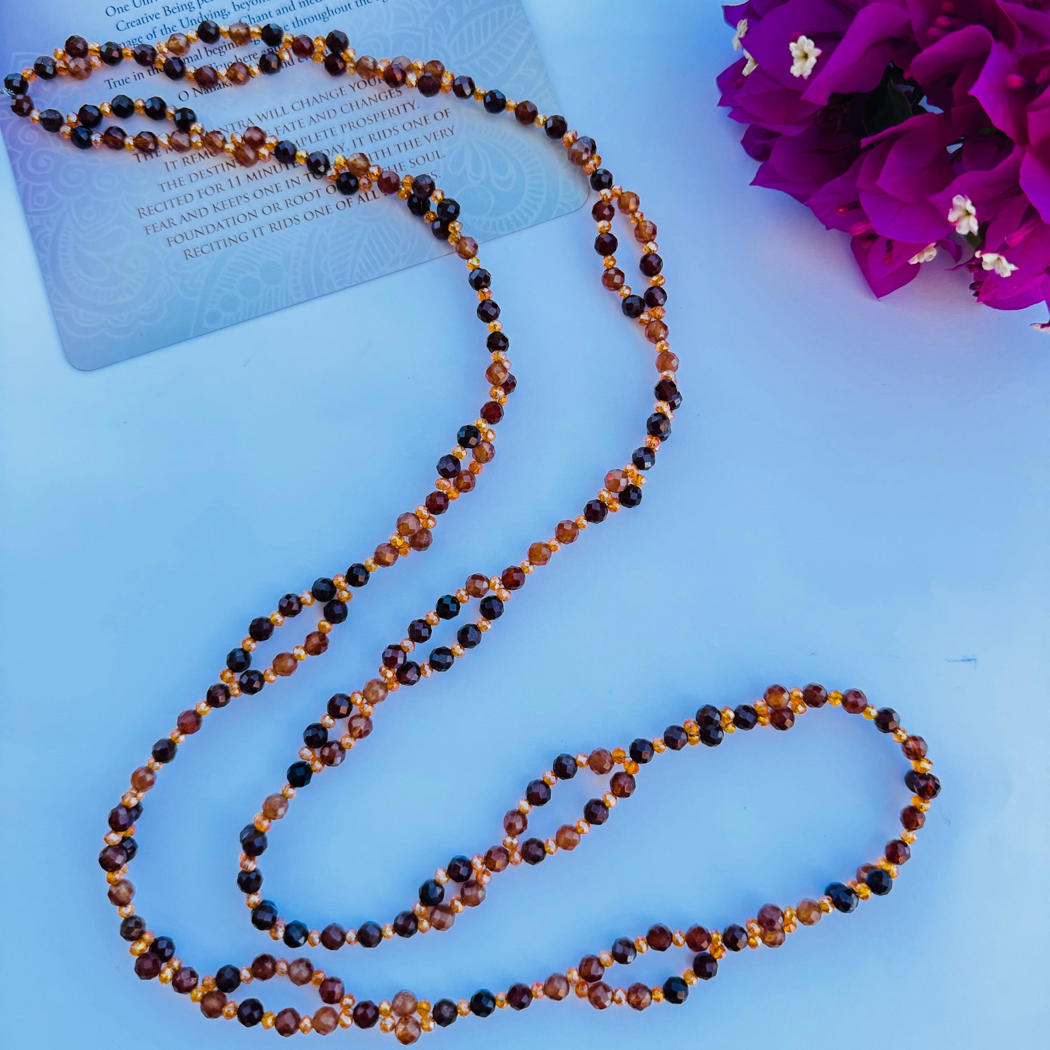 beaded orange and brown tantric necklace decorated with pink flowers on white surface