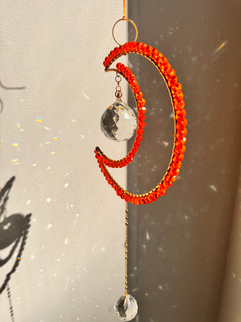 Decorative hanging ornament with orange beads and crystal-like elements on a neutral background