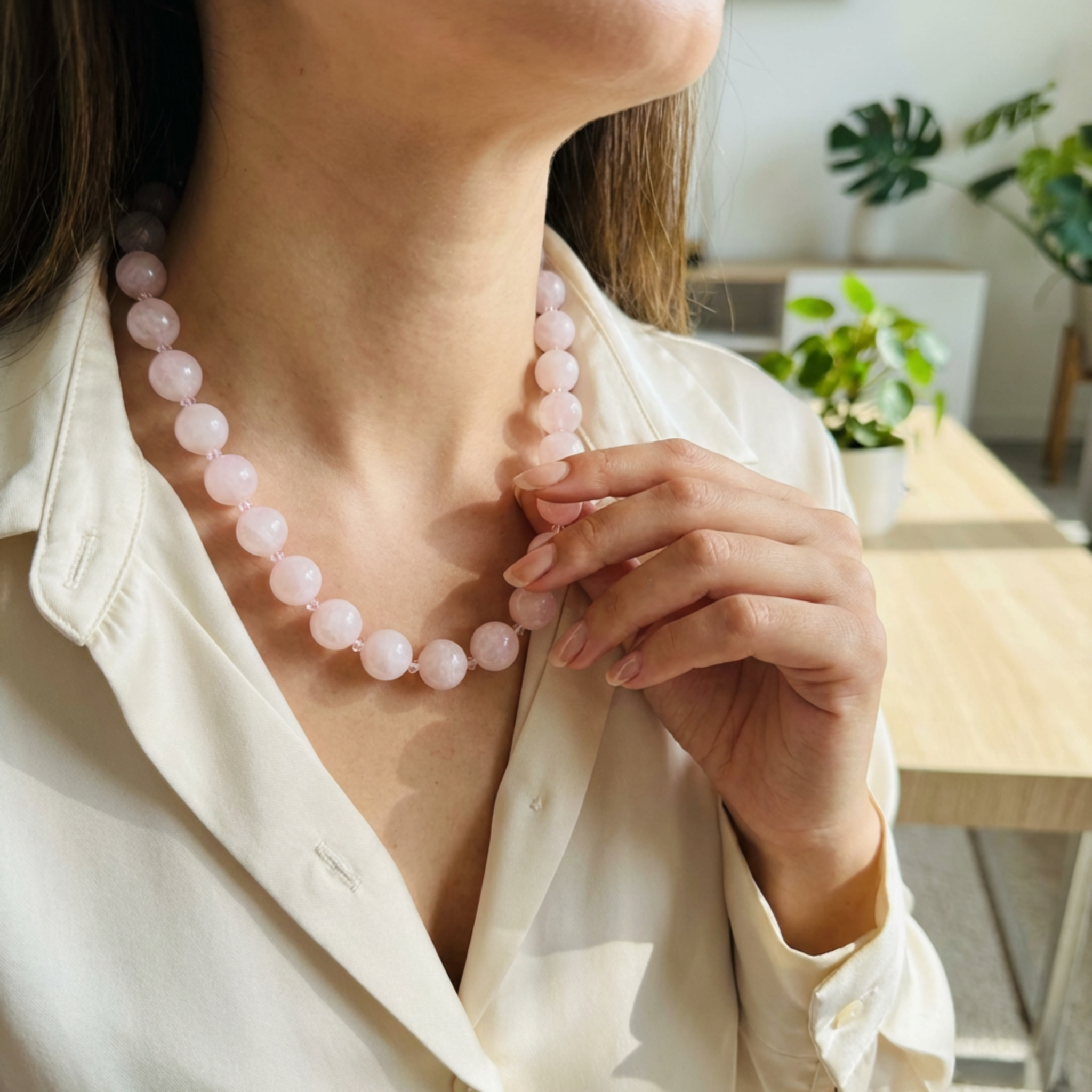 Person wearing a pink beaded necklace in an indoor setting with plants.