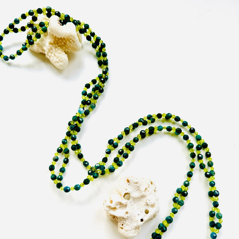 green and light green beaded necklace on white surface decorated with sea shell