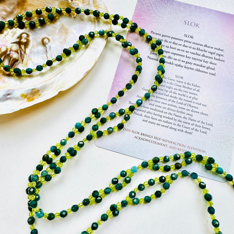 beaded green gemstone necklace on white surface decorated with big seashell and a mantra card