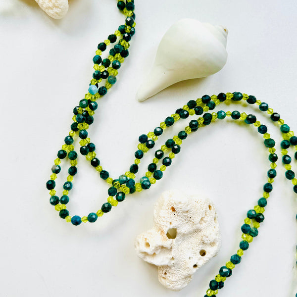 A tantric mala necklace with green gemstones and a white shell bead, displayed on a white background.