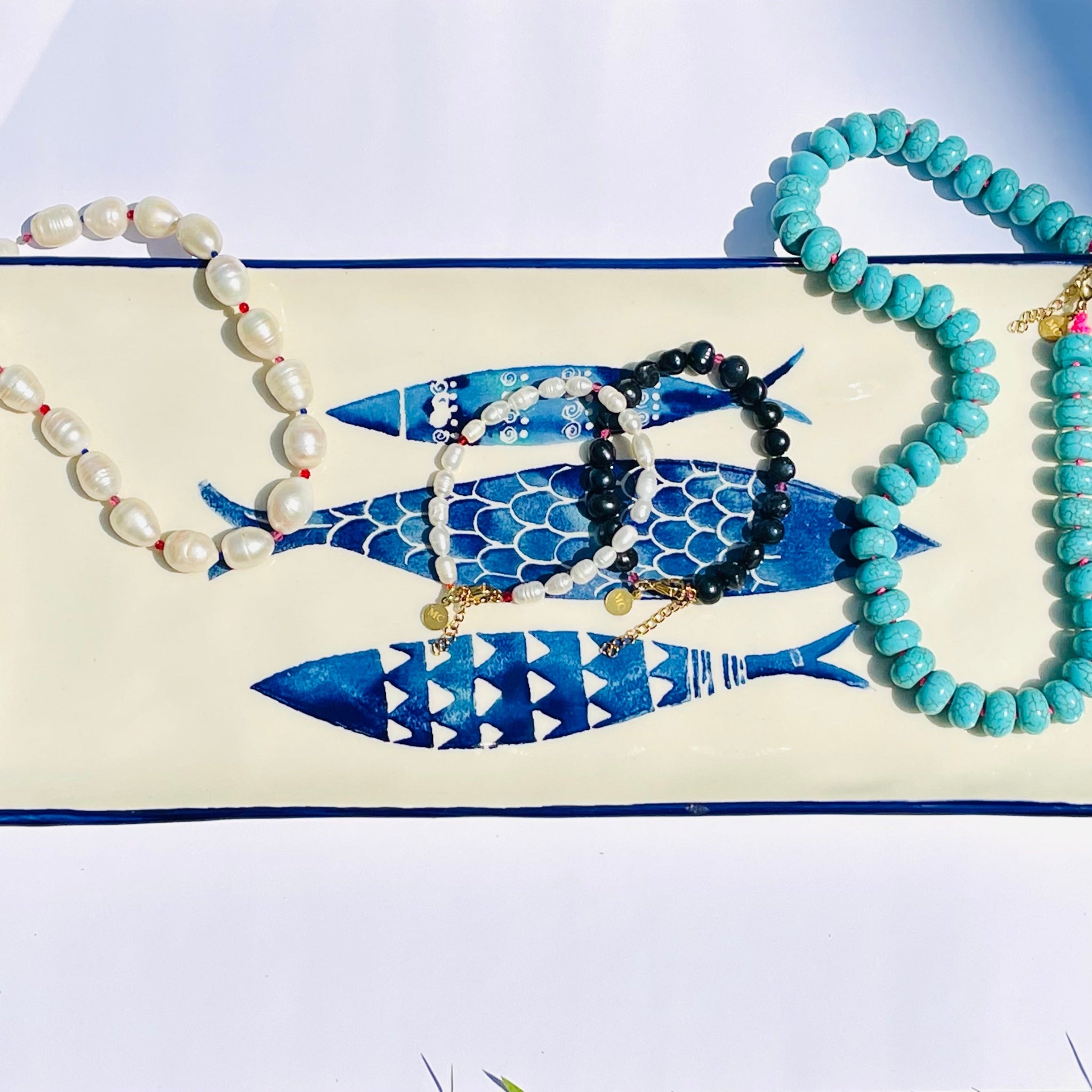 pearl necklace, pearl bracelets and turquoise beaded necklace on white plate with fish prints