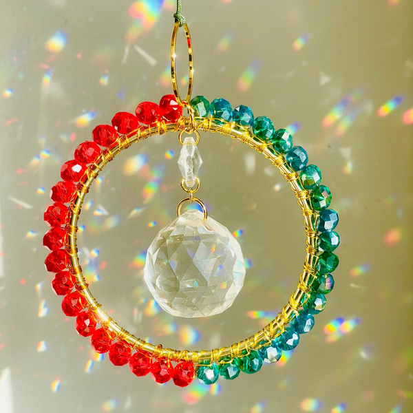 Crystal ornament half red half ocean color wire wrapped around a circle brass with prism in the middle creating rainbows in front of white wall