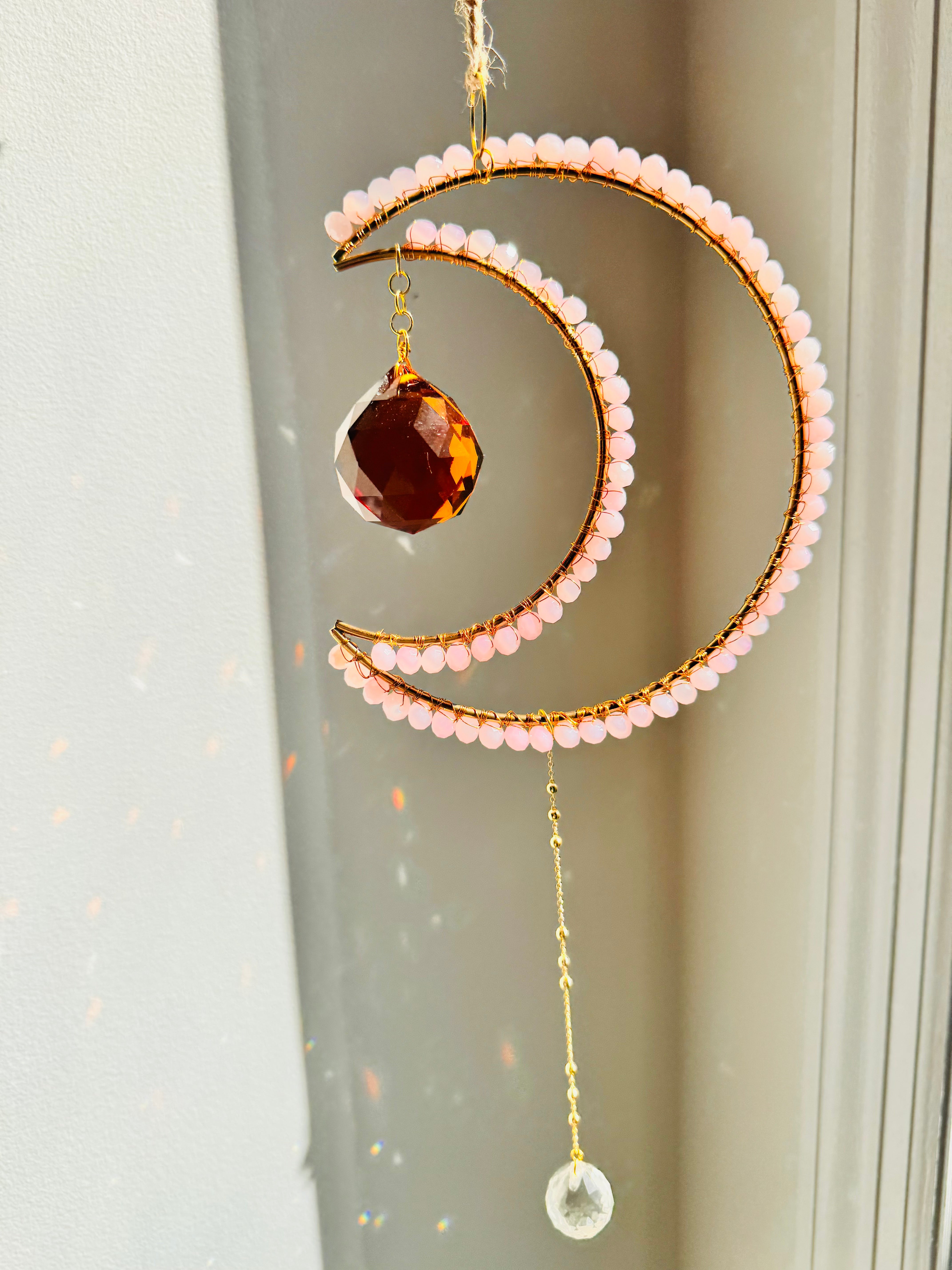 Decorative hanging moon and crescent moon with beads and crystals against a neutral background
