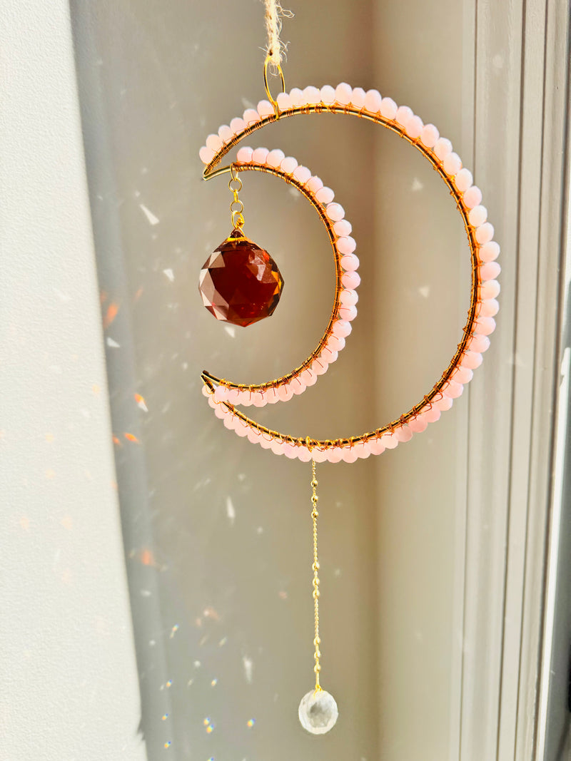 Decorative hanging ornament with pink beads and a red gemstone on a light background