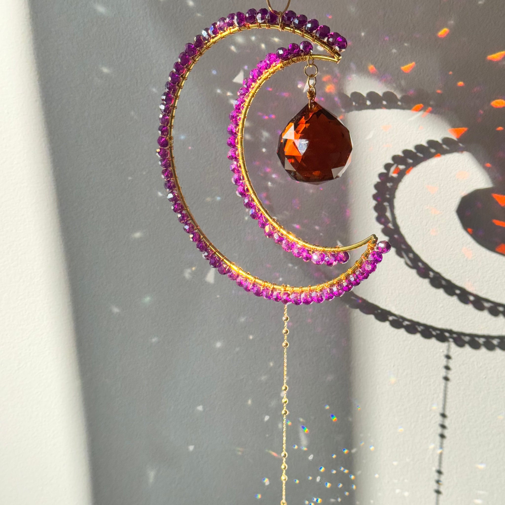 Decorative moon-shaped ornament with purple beads and a brown gemstone on a gray background.