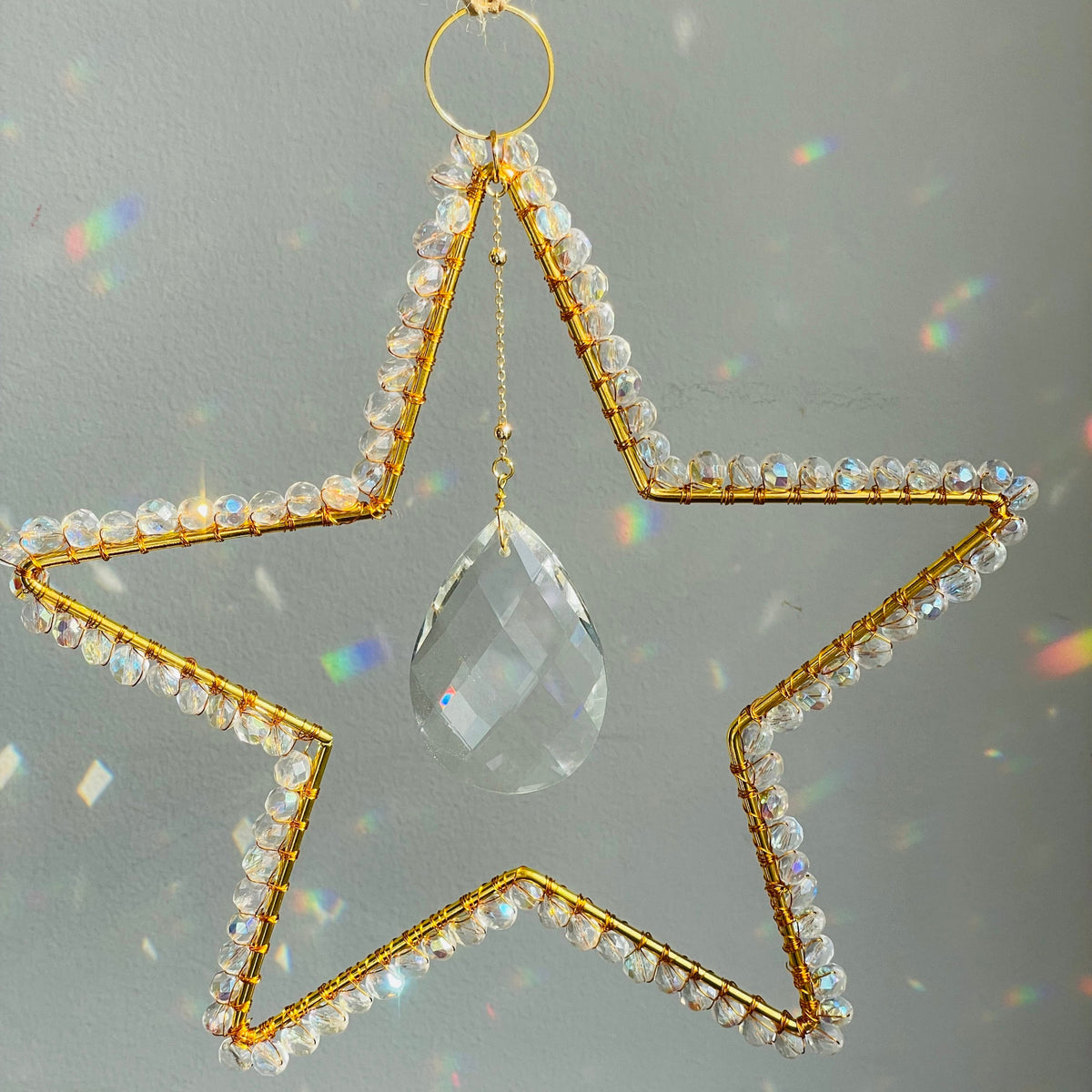 A clear suncatcher with gold-colored metal rings and threads, shaped like a star, with a small crystal in the center.