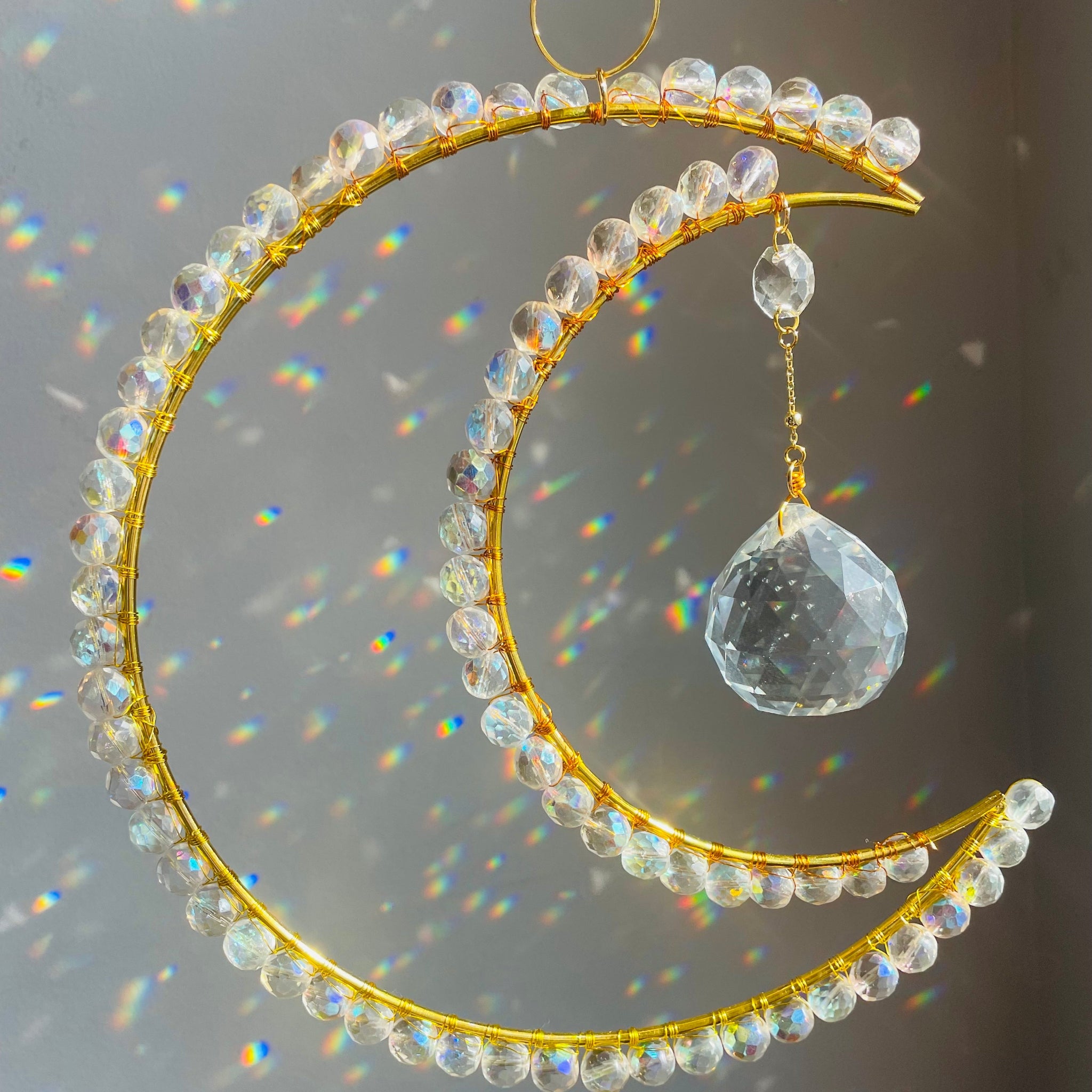 gold crescent wrapped with clear crystals with a big prism hanging in the middle creating rainbows