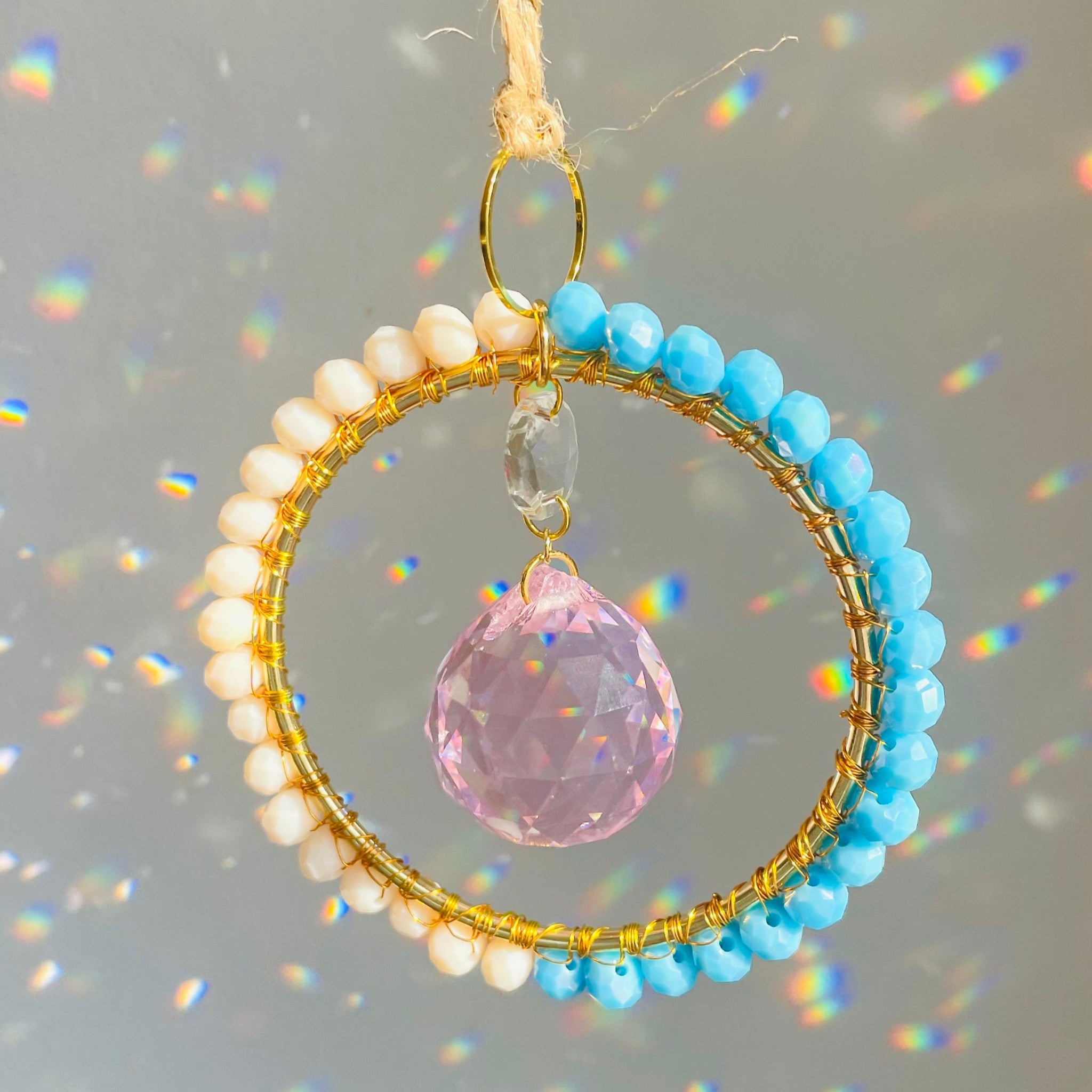 Decorative hanging ornament with blue and gold beads and a pink crystal on a gray background.