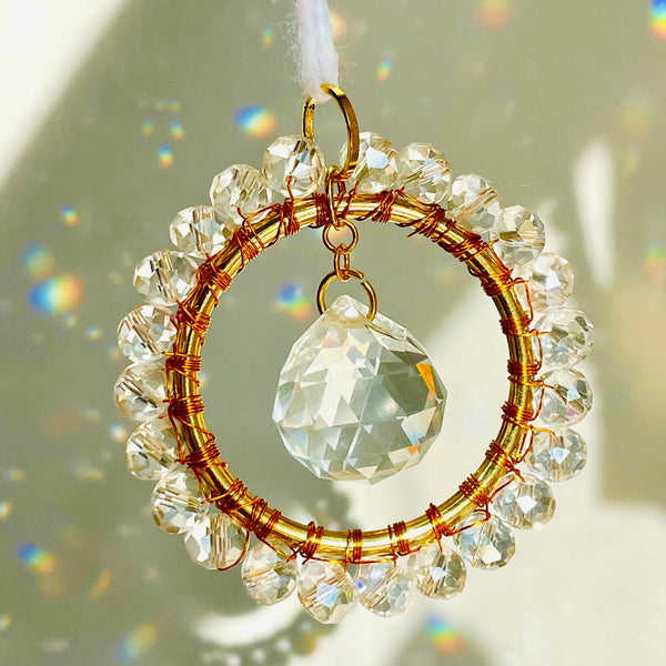 A mini circle suncatcher with a golden frame and clear crystal pendants hung from a chain.