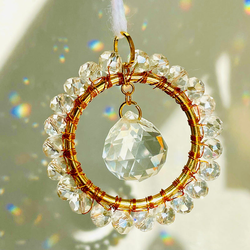 A mini circle suncatcher with a golden frame and clear crystal pendants hung from a chain.