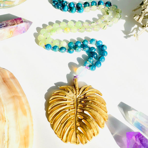 Colorful beaded bracelets and a gold leaf pendant on a white surface with crystals.