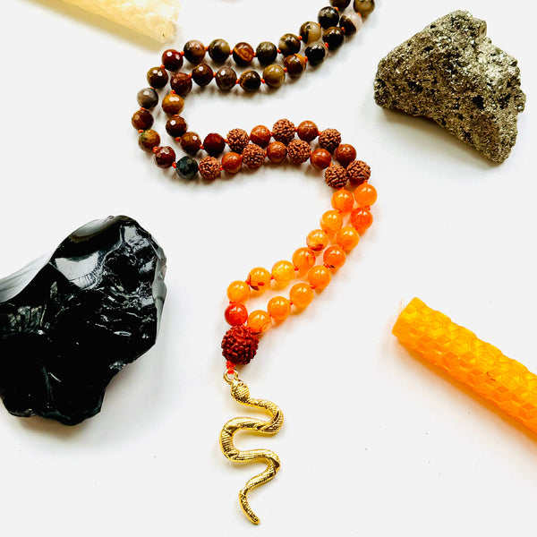 A collection of beaded necklaces with a brass serpent pendant, displayed alongside various gemstones and natural elements.