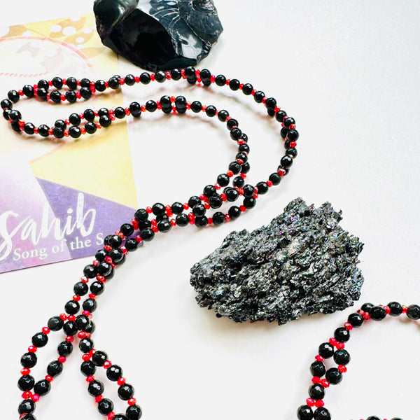 beaded red and black gemstone necklace with black crystal on white surface
