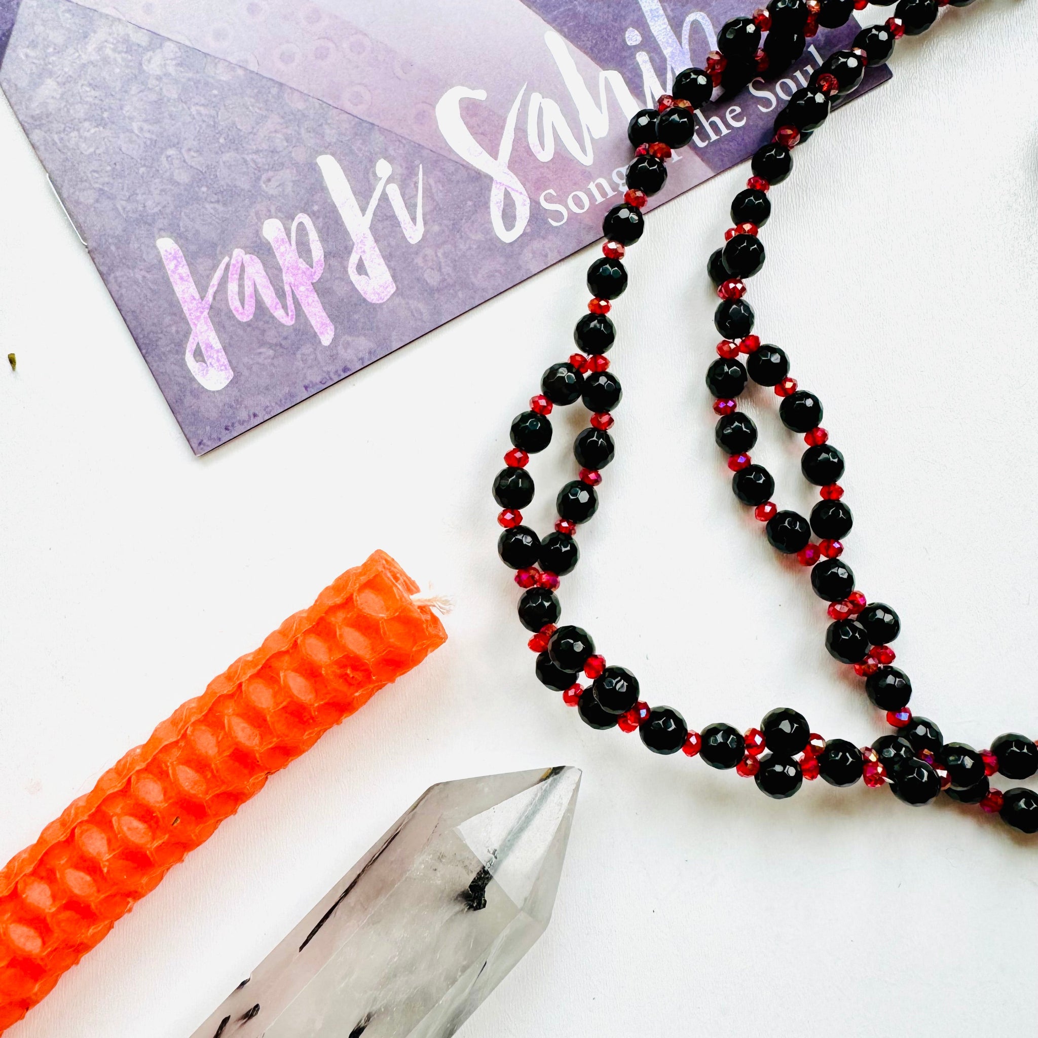beaded black and red gemstone necklace with orange candle and tower crystal