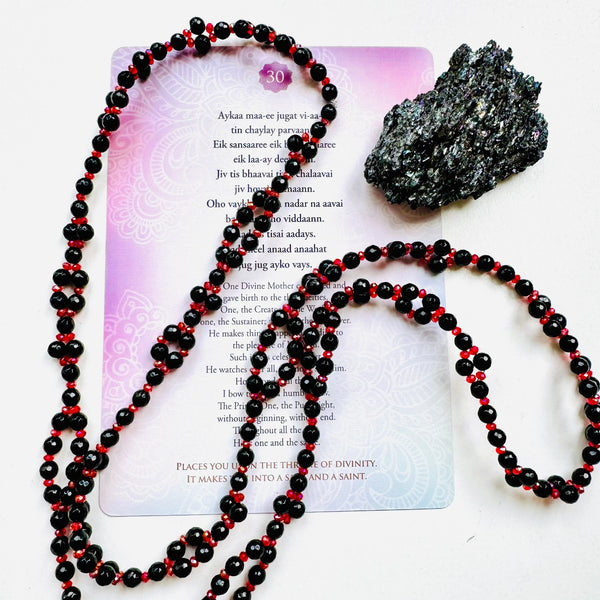 A black obsidian pendant with a red and clear beaded necklace, placed on a white surface with a purple text card that contains poetry.