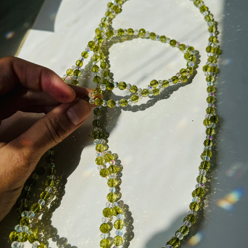 Green beaded necklace held by a hand on a white surface