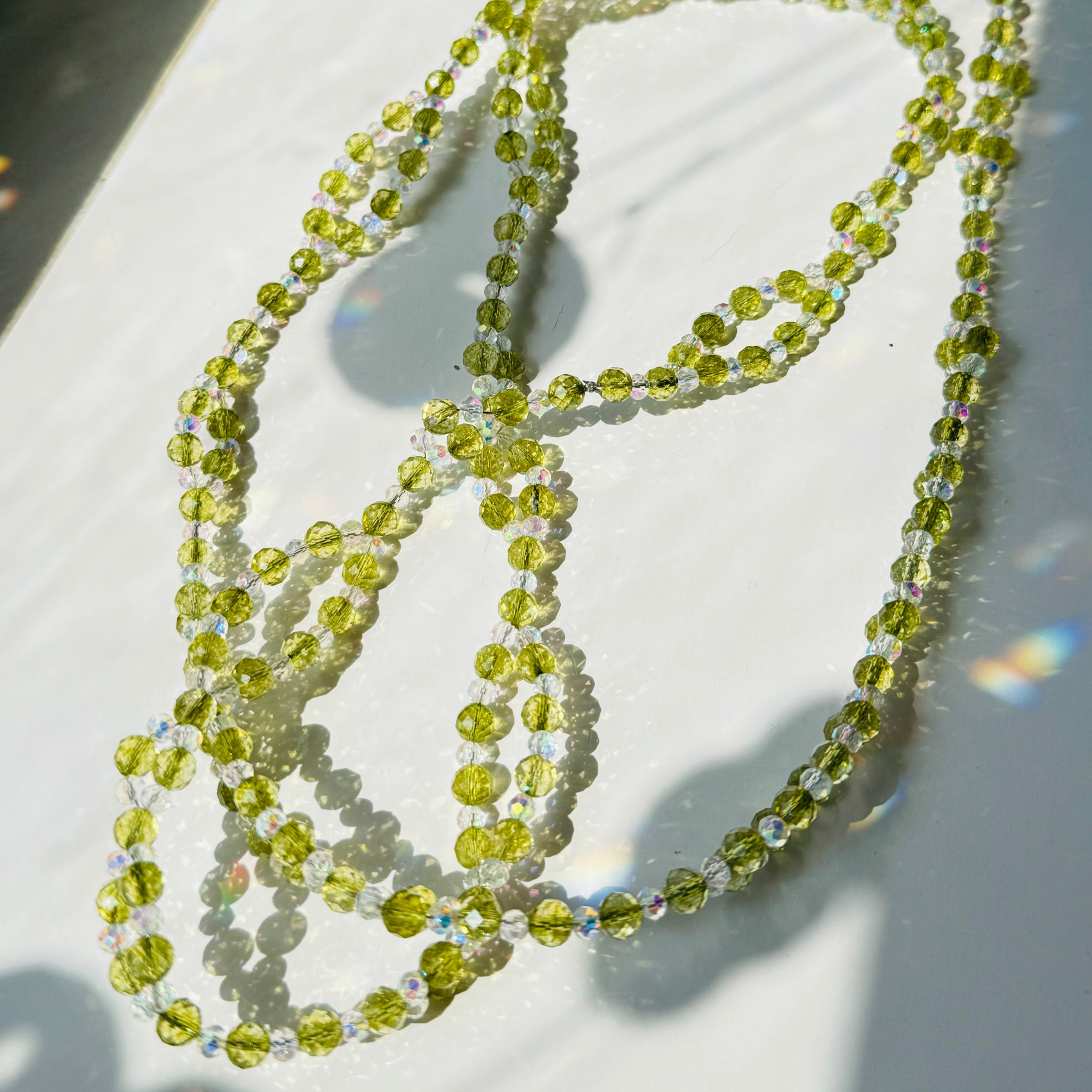 peridot gemstone and clear crystals beaded creating a necklace on white surface