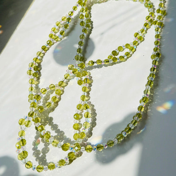 peridot gemstone and clear crystals beaded creating a necklace on white surface