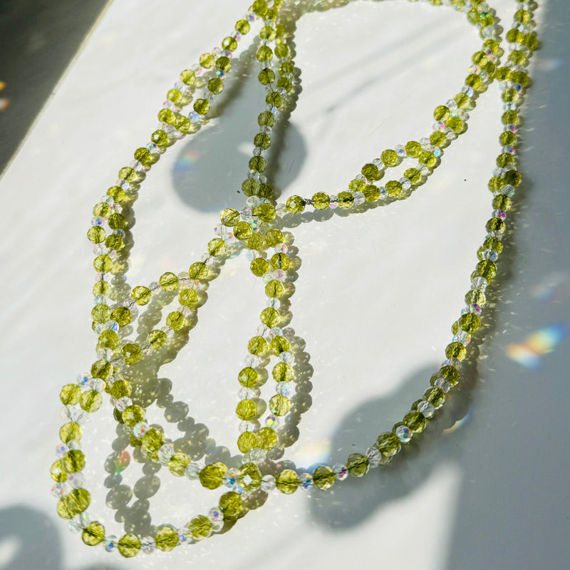 peridot gemstone and clear crystals beaded creating a necklace on white surface