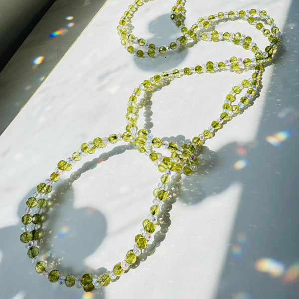 Peridot green gemstone beaded with clear crystals on white surface