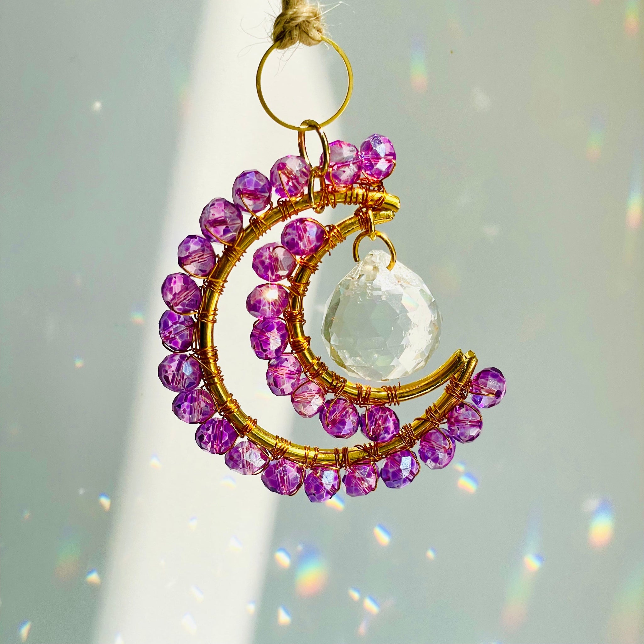 Decorative hanging ornament with purple beads and a clear crystal on a light gray background