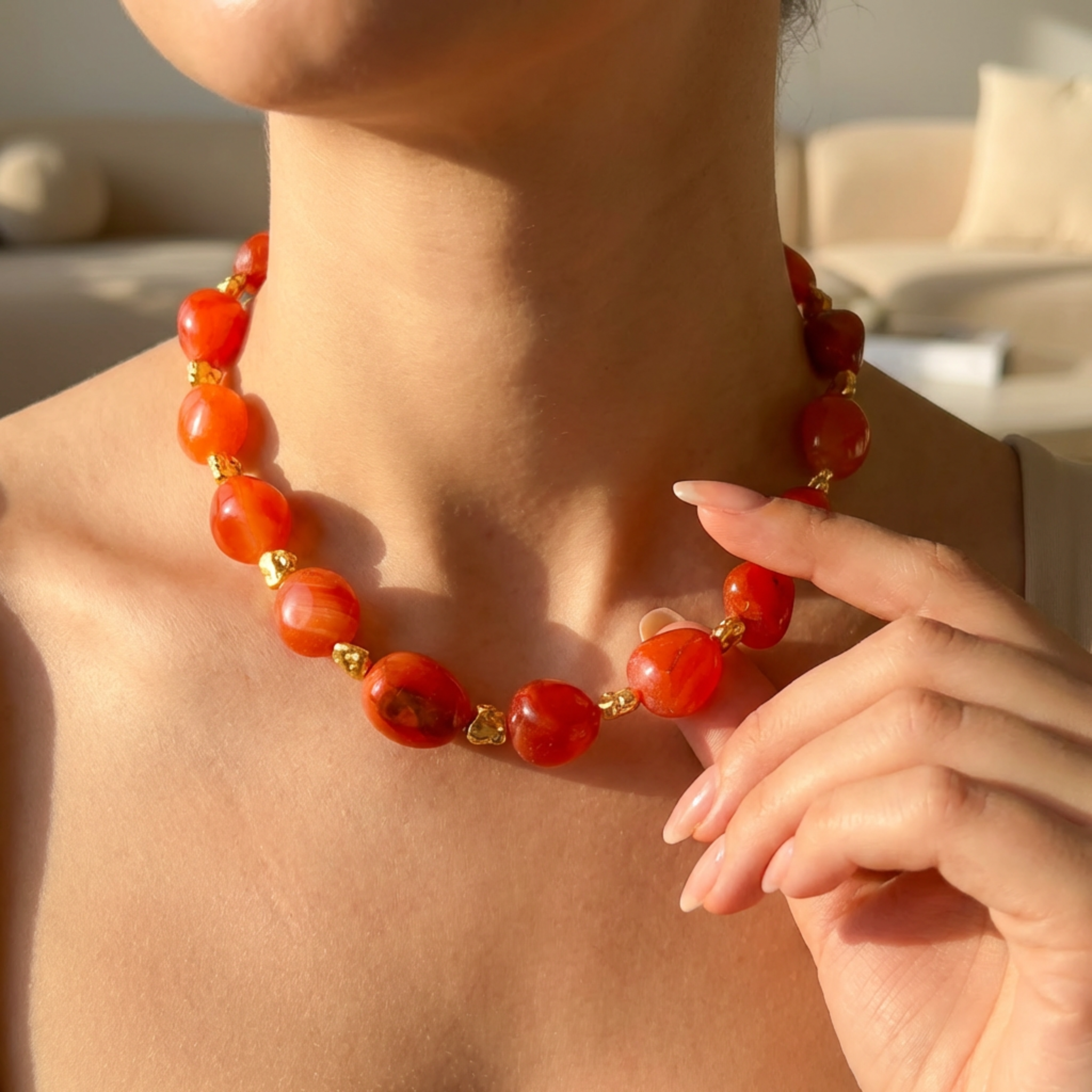 Person wearing a red beaded necklace with gold accents, held by a hand.