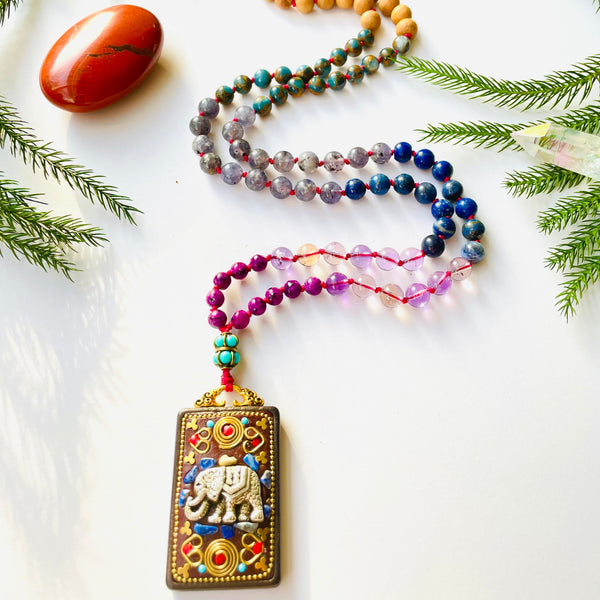 beaded gemstone necklace with elephant pendant on white surface with red gemstone and pine needles