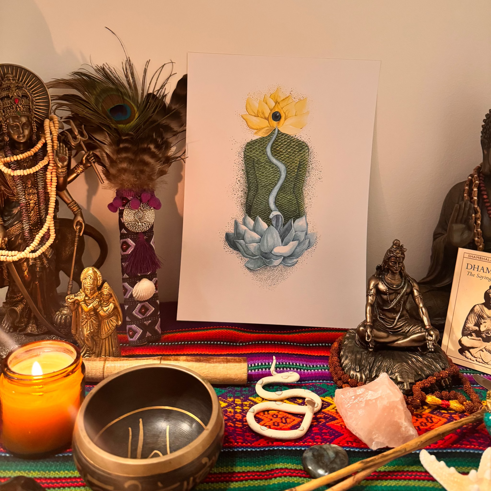 Altar setup with various items including a candle, bowl, and artwork on a colorful cloth.